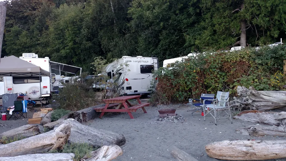 Campers, picknicktafels, campingstoelen en drijfhout langs de kust van Beachcomber