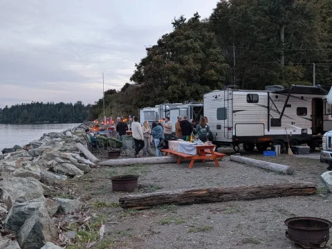 Guests gathering beside waterfront RV sites and picnic tables at Beachcomber RV Park in the evening