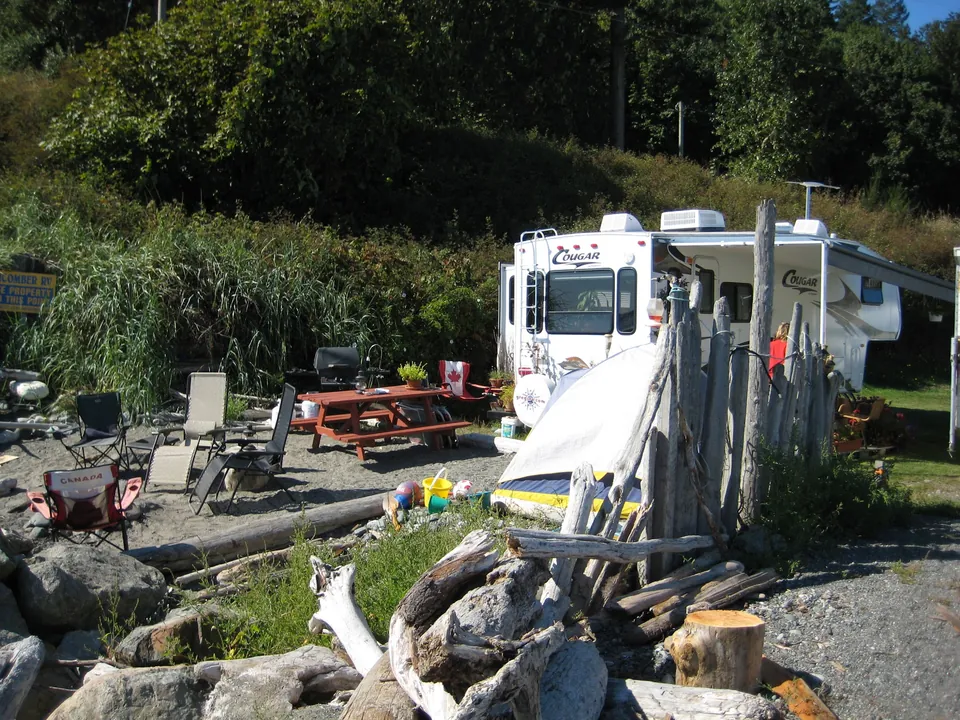 Een camperplaats met een klein bijzettentje, picknicktafel en drijfhout bij Beachcomber RV Park
