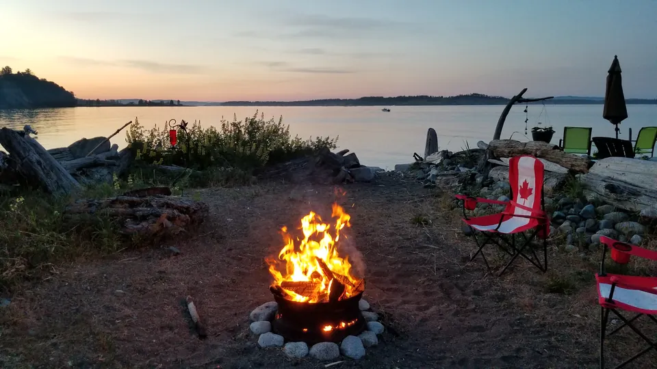 A campfire and red camping chairs beside calm water at sunset at Beachcomber RV Park
