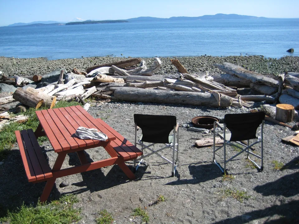 Two camping chairs and a red picnic table facing the ocean at Beachcomber RV Park